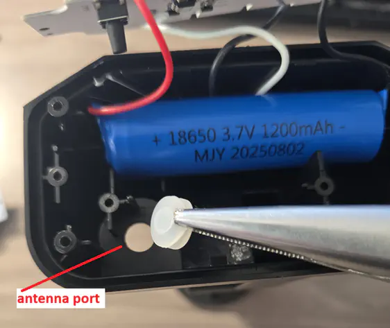 Tweezers grabbing rubber switch grommet and “Antenna port” pointing to the now exposed hole